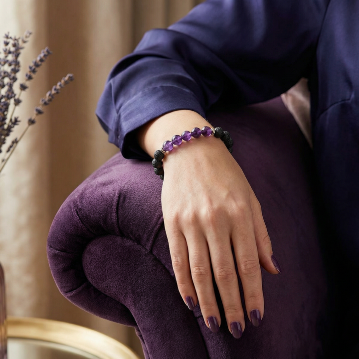 Person wearing a purple amethyst and lava stone beaded bracelet on a purple cushion with lavender in the background